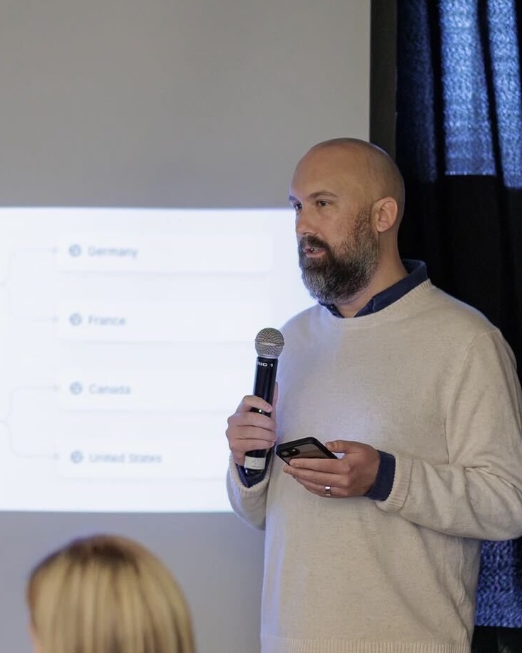 Barrett Ahern speaking at the Vervaunt Pulse Breakfast, holding a microphone while presenting to attendees with a slide showing international market priorities projected behind him